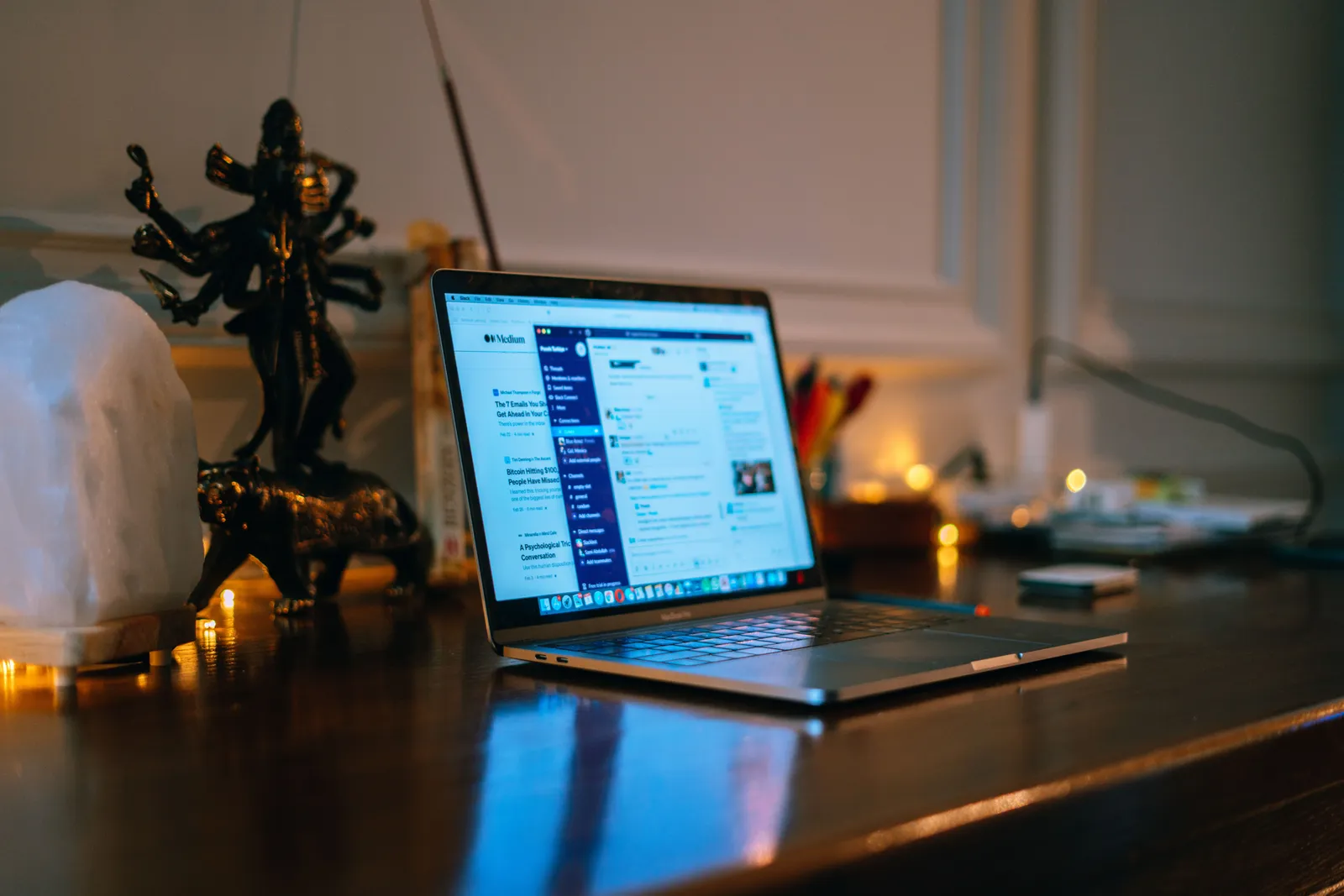 A cozy home office setup with a laptop on a wooden desk surrounded by warm lighting and decor