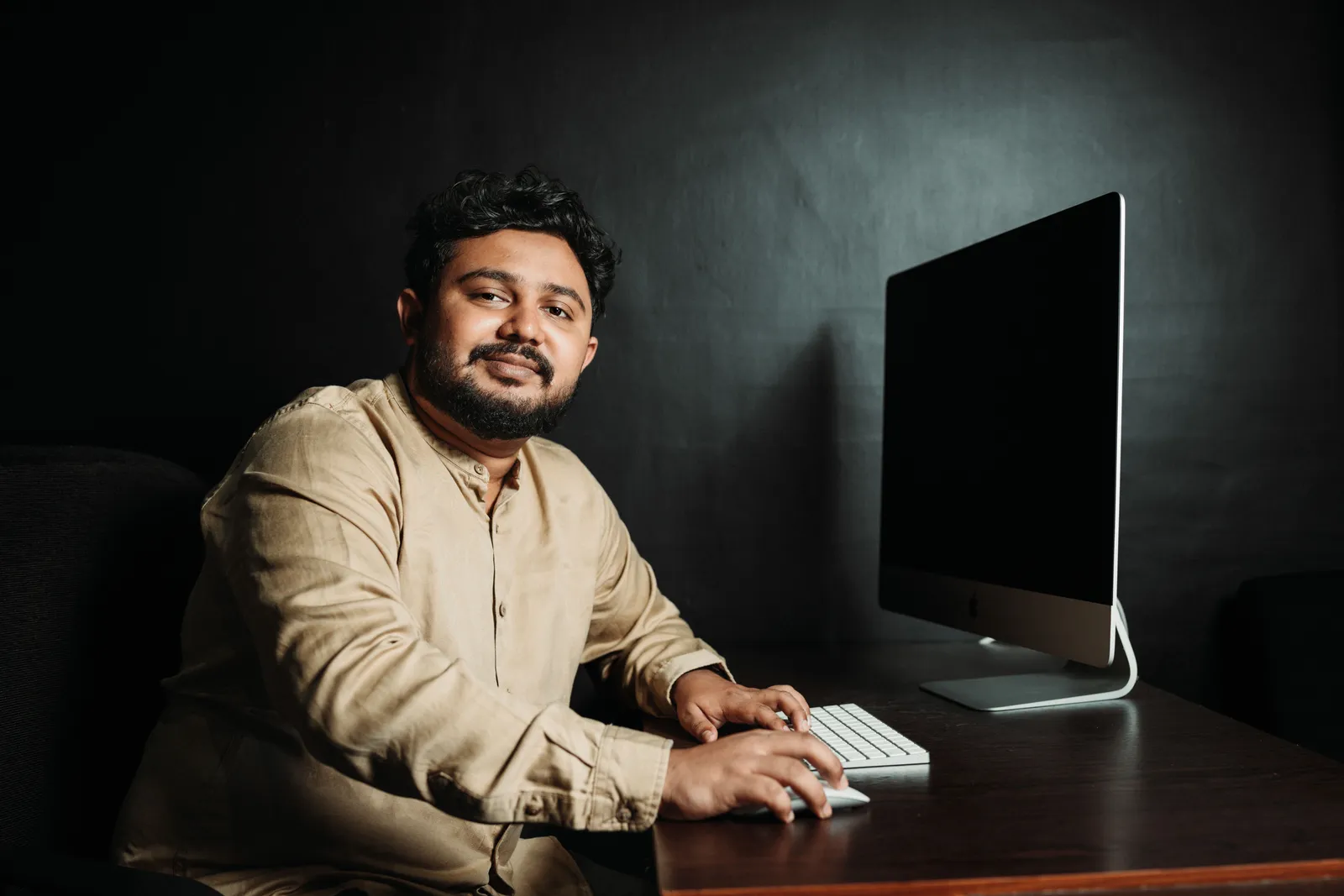 Portrait of a man working at a desk with a computer, in a dimly lit office setting
