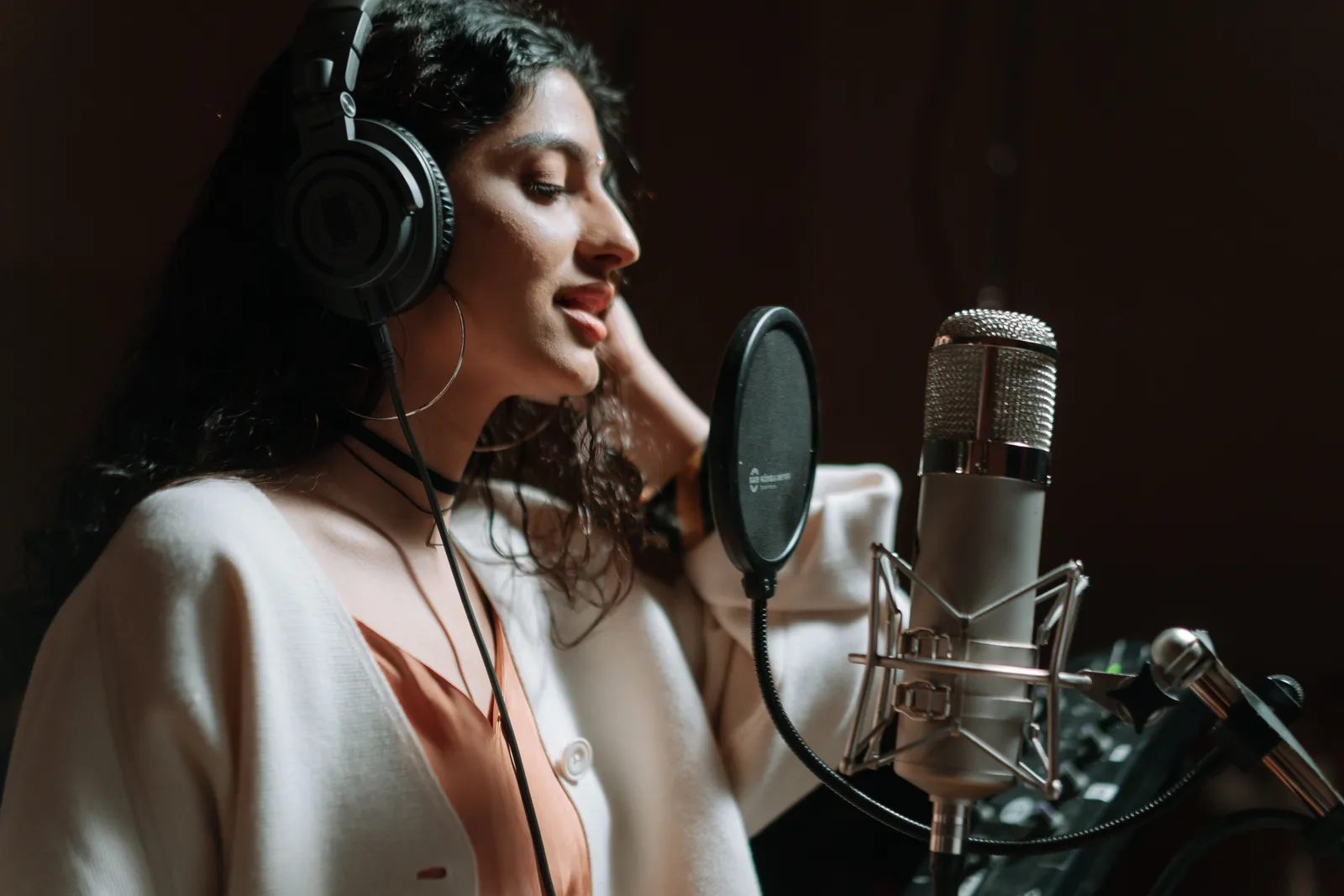 Woman in a music studio singing into a microphone, wearing headphones
