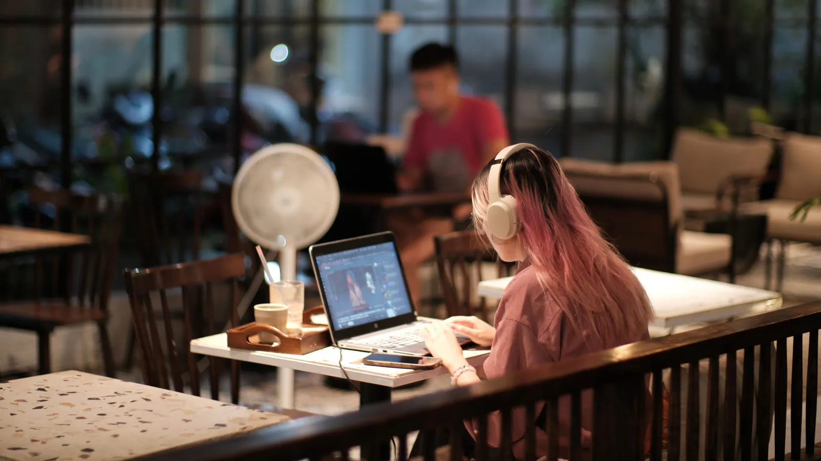 A woman with headphones edits a video on her laptop in a cozy caf茅 environment, Vietnam