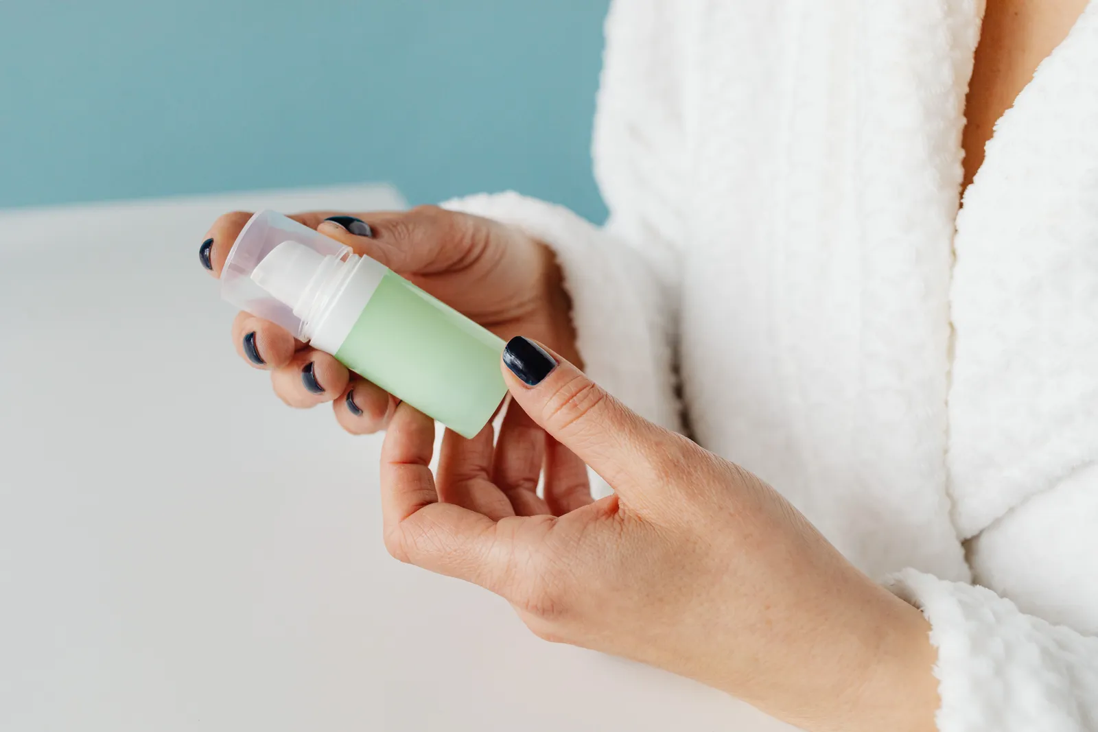 A person in a bathrobe holding a skincare product, focusing on hands and bottle
