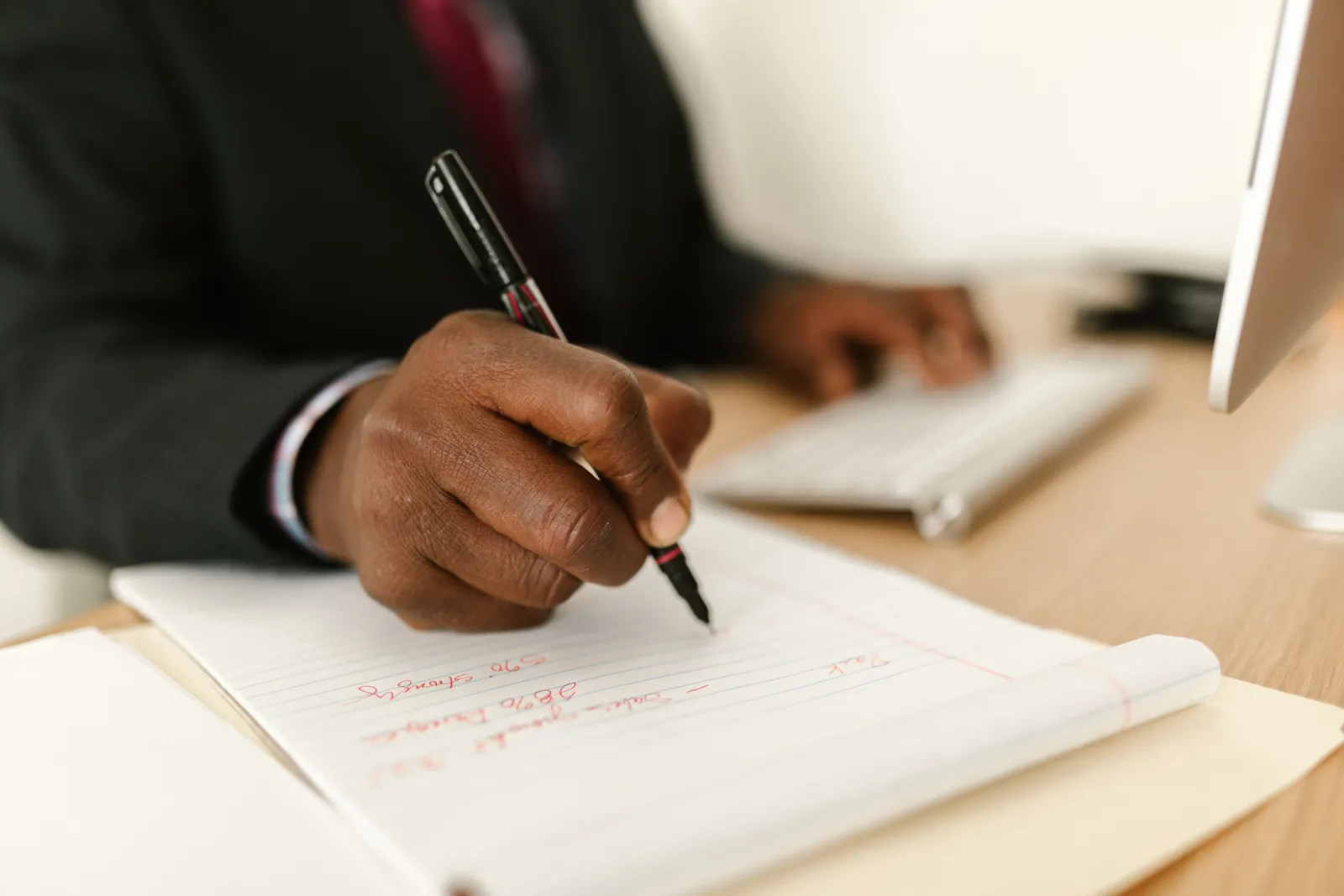 Close-up of a businessman writing notes in a notepad at a desk, highlighting stationary and productivity
