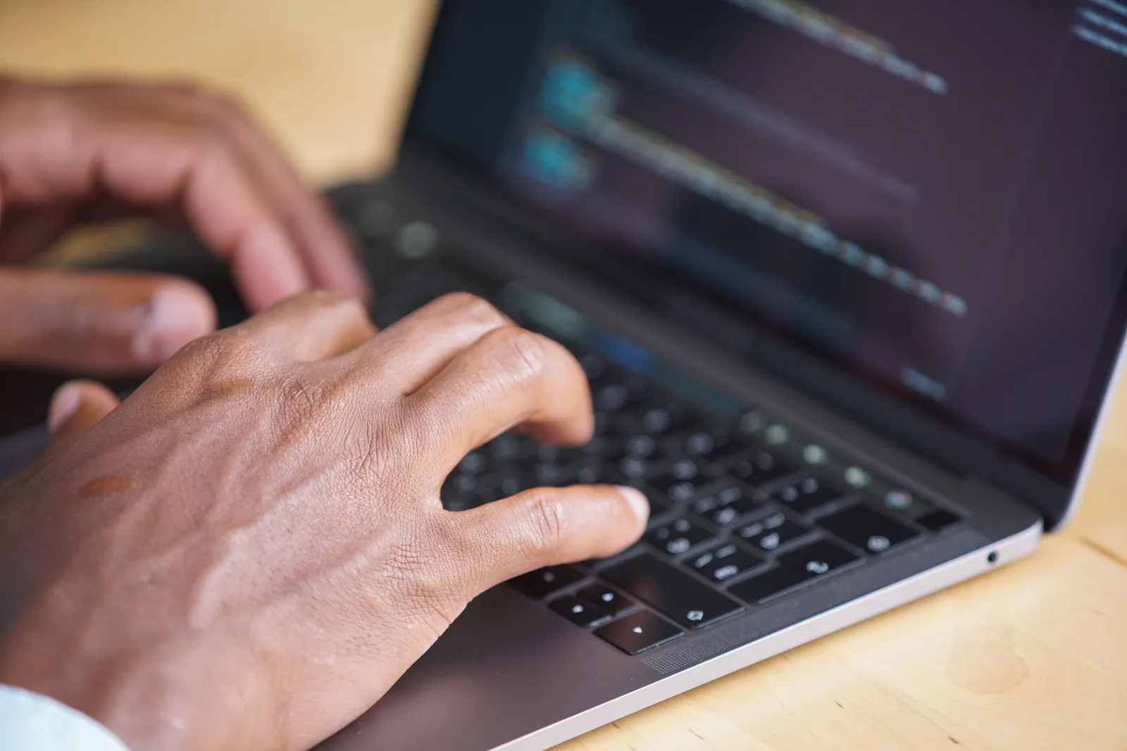 Hands typing on a laptop with code displayed on screen, showcasing technology use