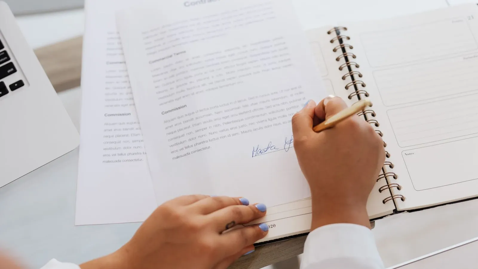 Hands signing a document beside office stationery