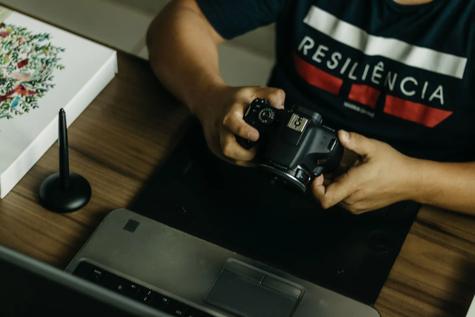 A person holding a DSLR camera at a creative workspace with a tablet and laptop