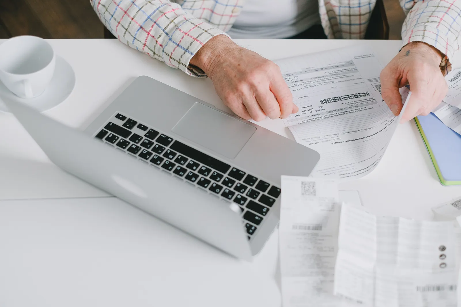 Close-up of hands organizing documents on a desk with a laptop