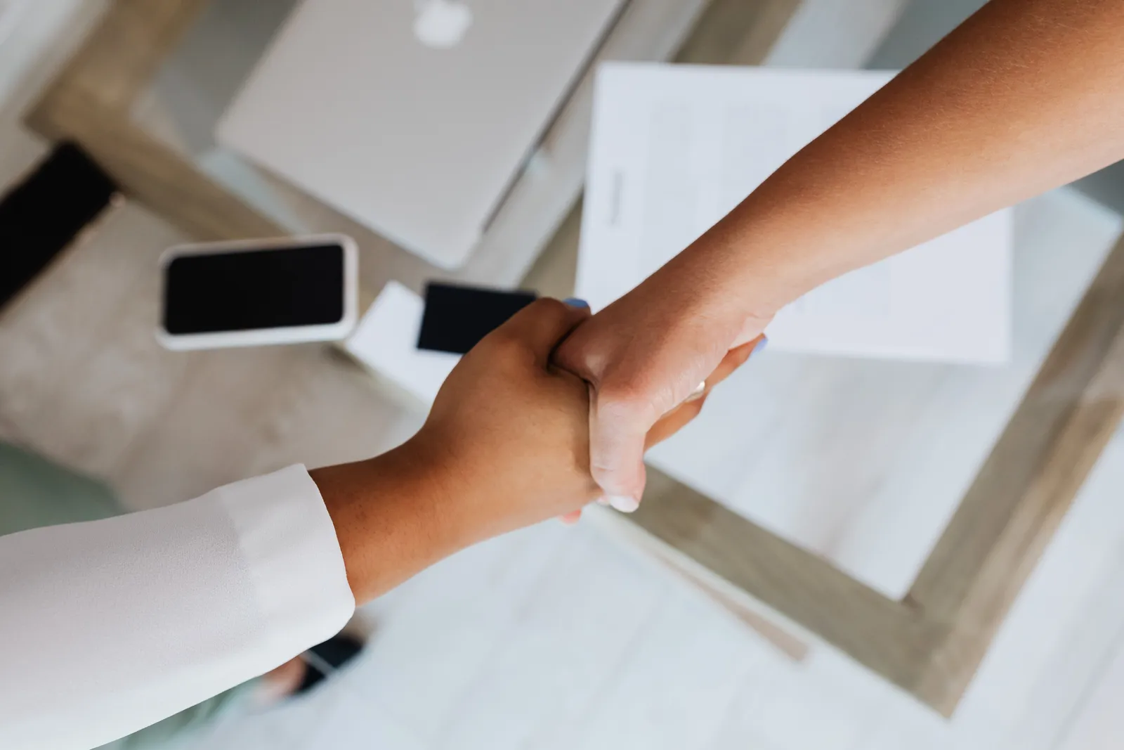 Two people shaking hands over a desk with modern tech, symbolizing a successful business agreement