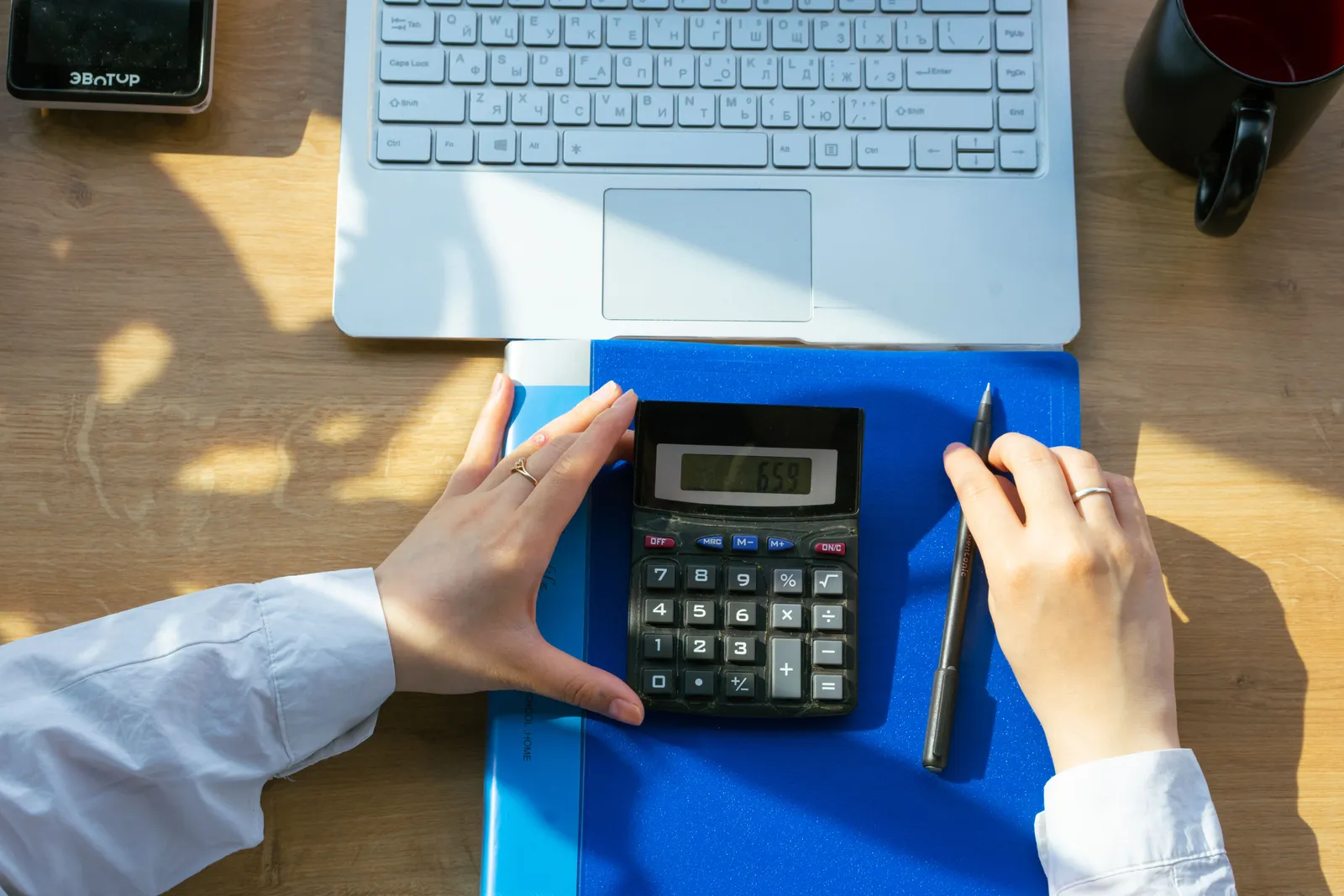 Hands using calculator on a desk with a laptop, pen, and notebook. Perfect for office or finance themes