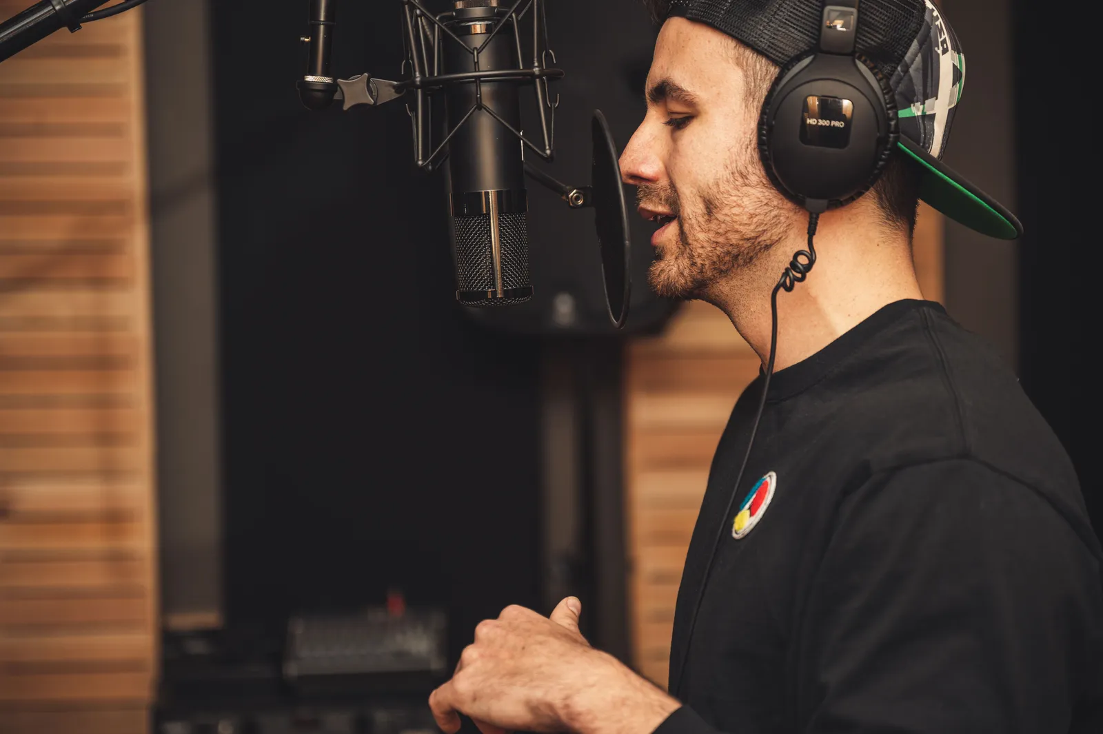 A man wearing headphones and recording vocals in a music studio with a microphone