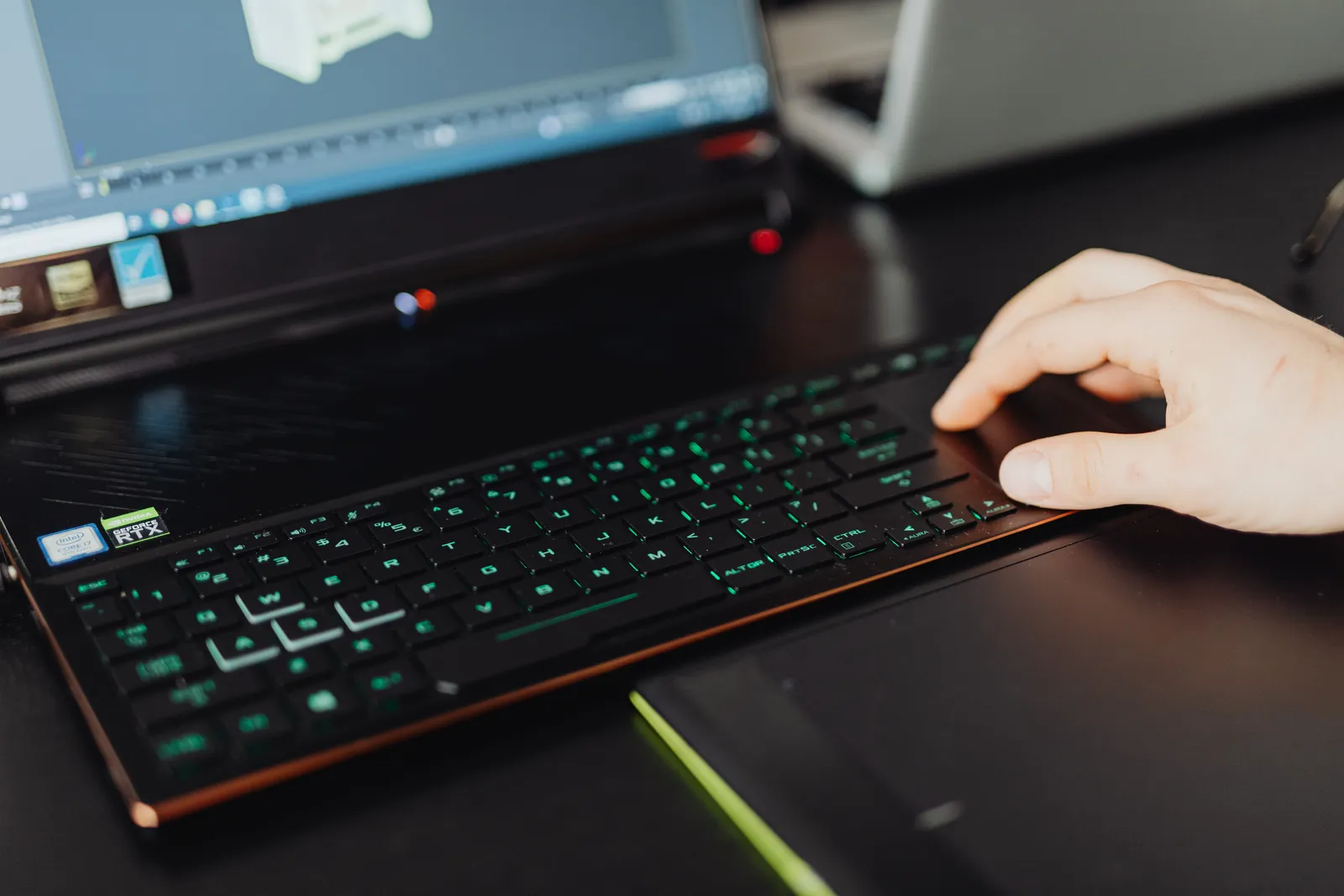 Close-up of a hand on a laptop keyboard working on a 3D modeling project with green LED keys