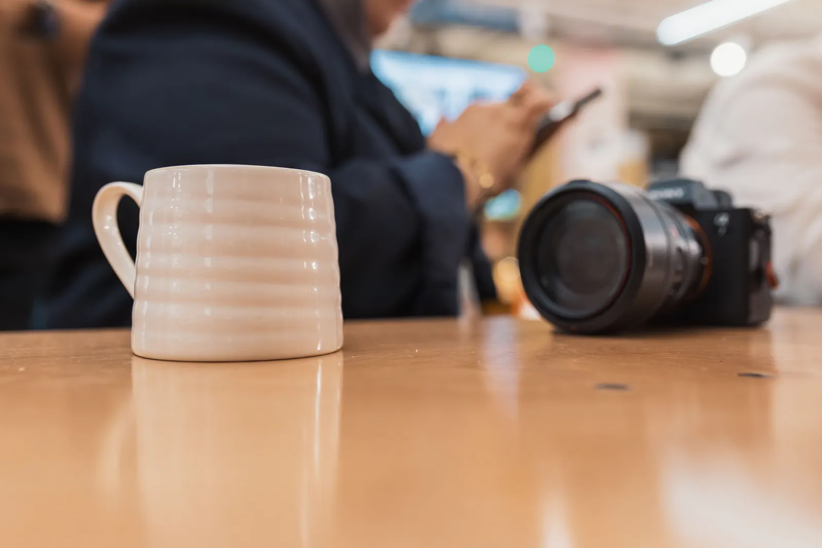 Coffee mug and camera on a table with blurred people in the background