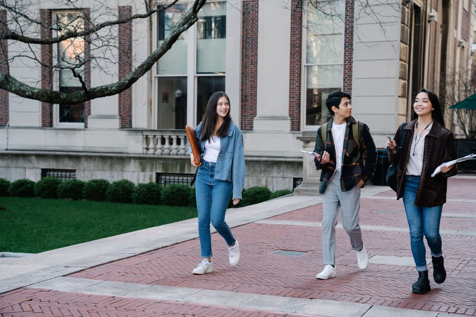 Group of young students walking on campus sidewalk on a bright day, showcasing casual university life