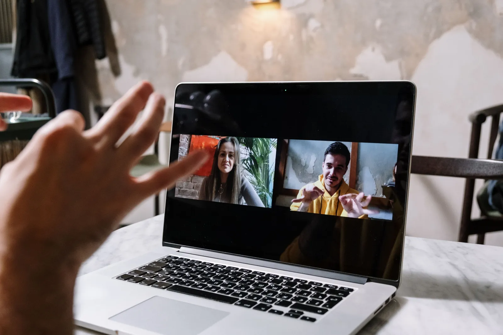 Hands gesturing during a video call on a laptop screen, showing two people in a virtual meeting