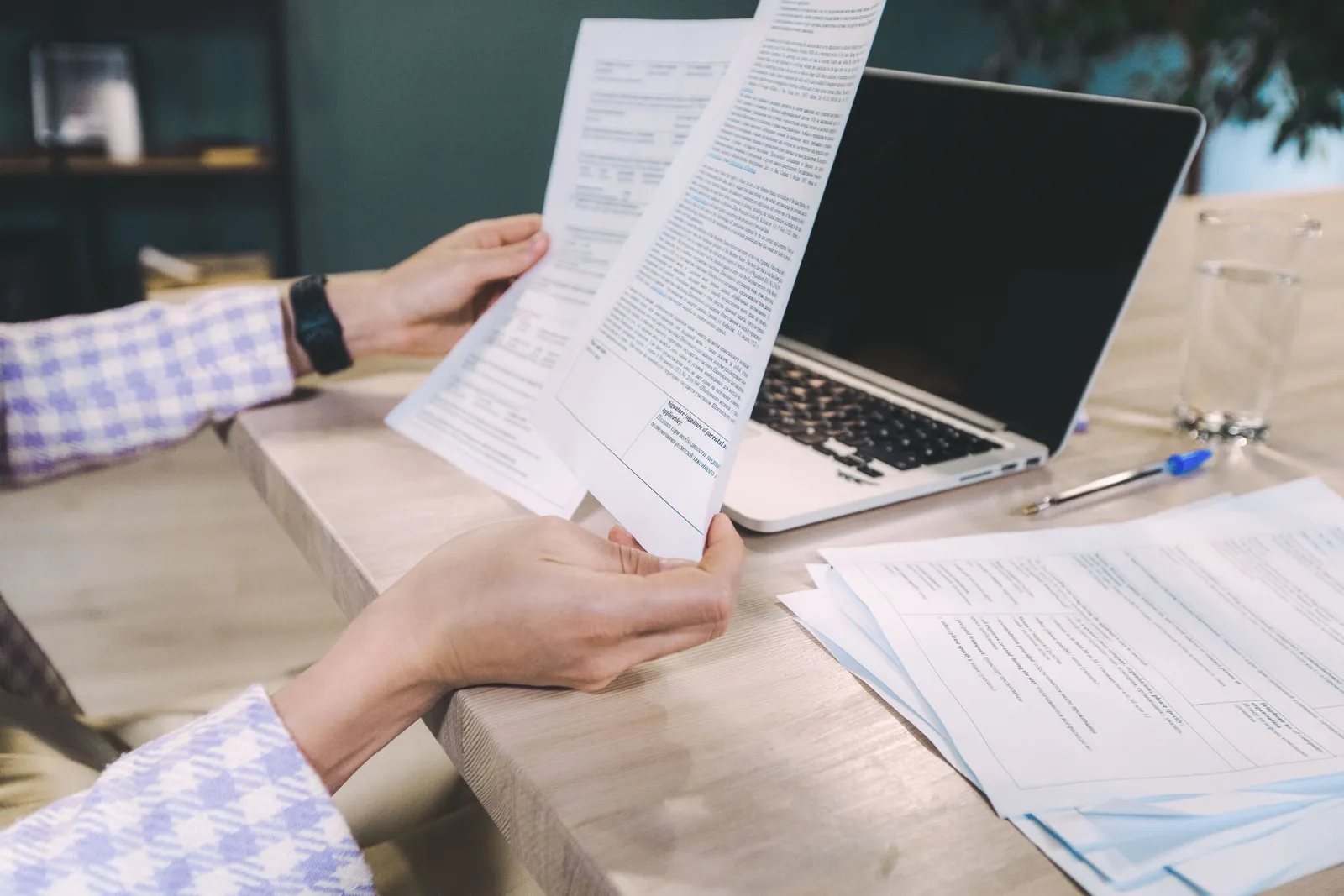 Close-up of hands examining printed documents next to laptop on office desk
