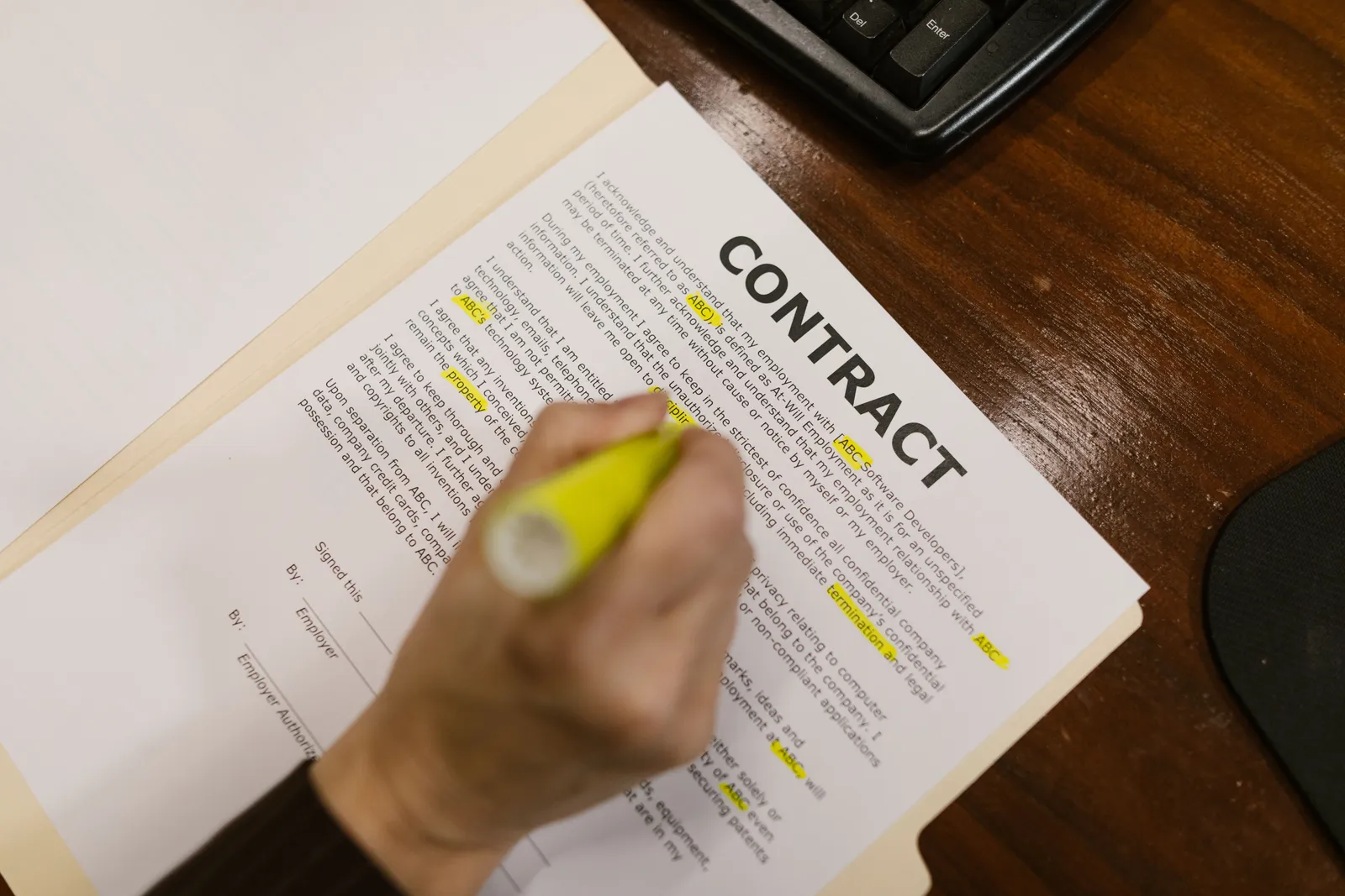 Focused view of a person highlighting text in a contract document on a wooden office desk