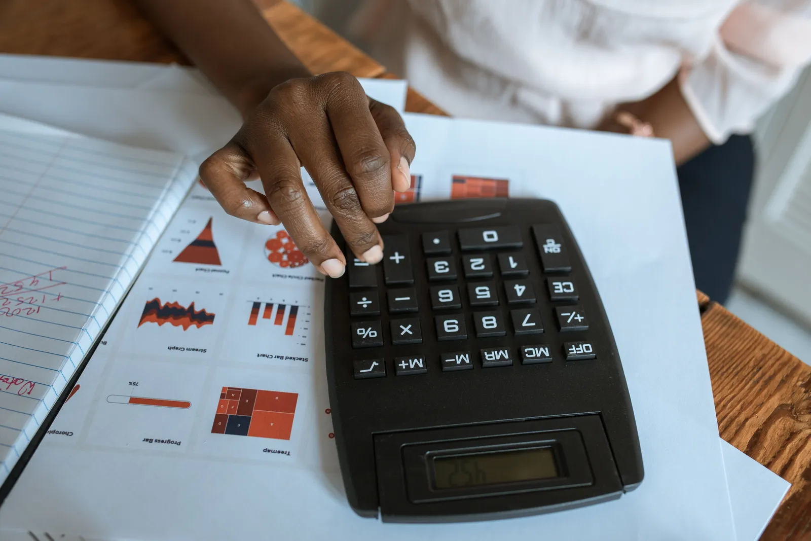 Person using calculator on desk with financial charts and graphs, ideal for business and finance themes