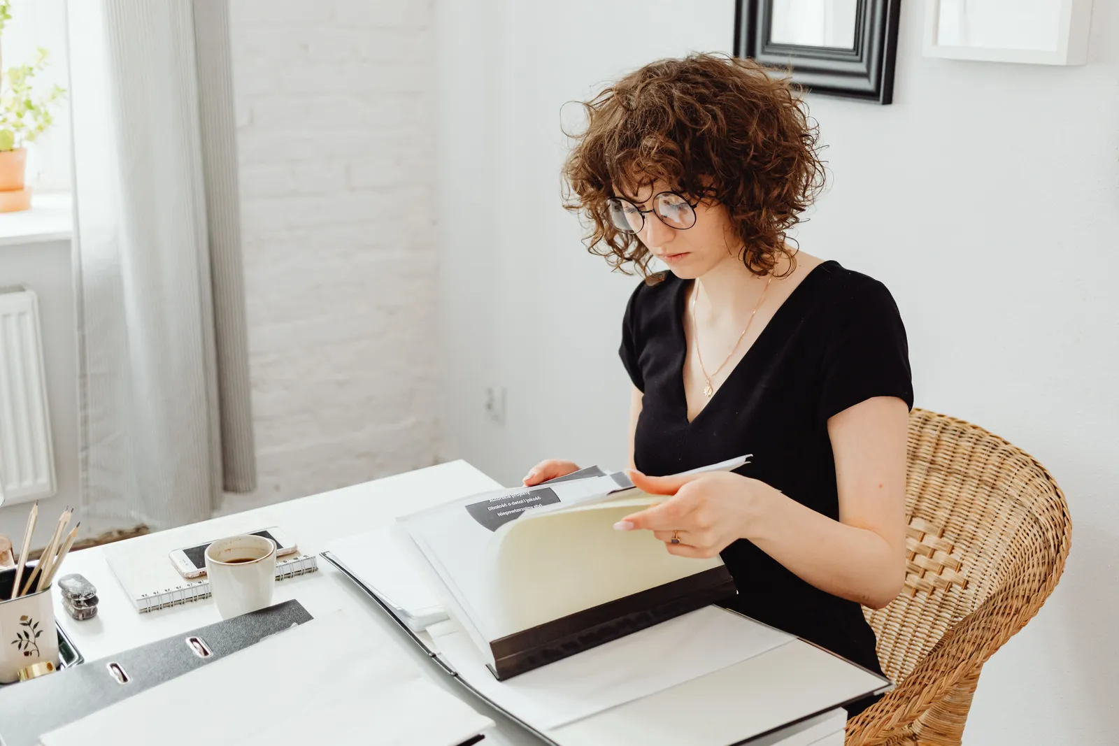 A woman in a black v-neck shirt reading documents while sitting at a desk in an office