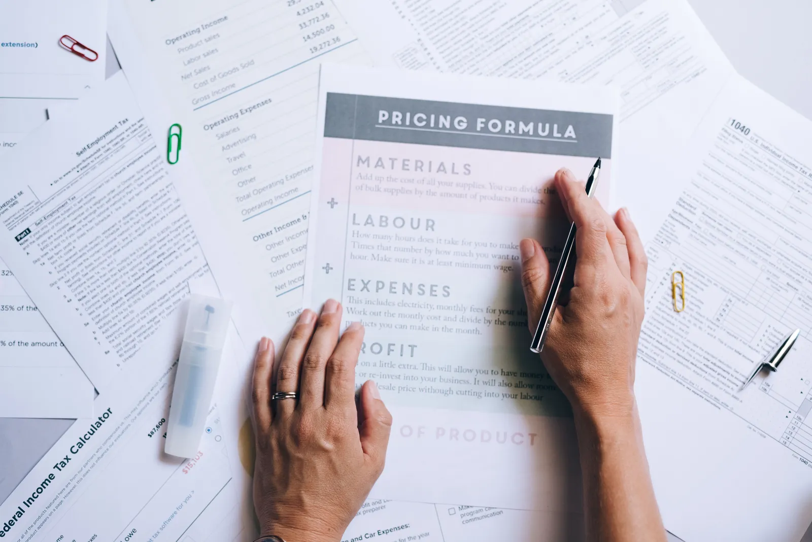 Hands organizing business documents and pricing formula papers on an office desk