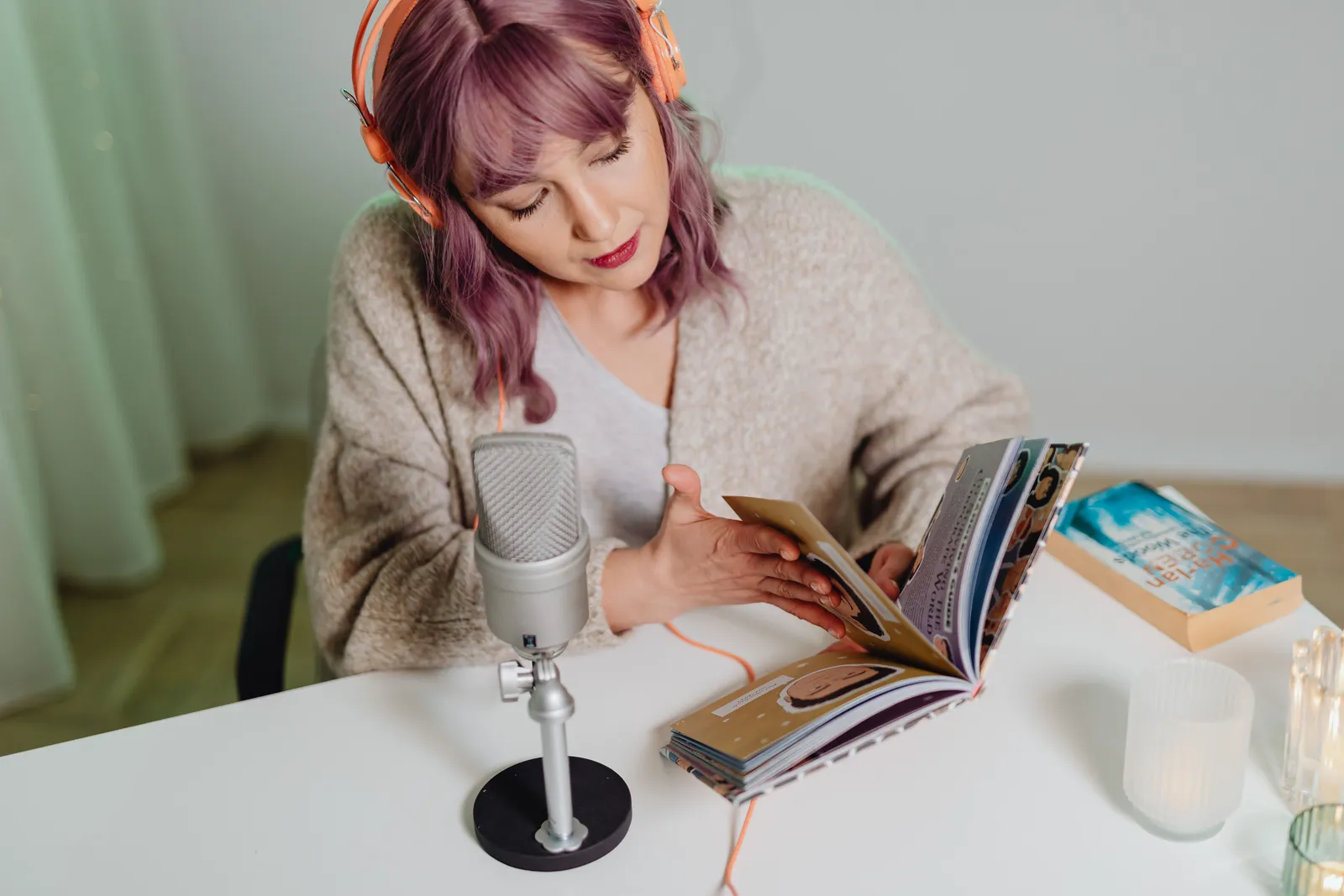 Young woman podcasting at a desk with headphones and books, using a microphone
