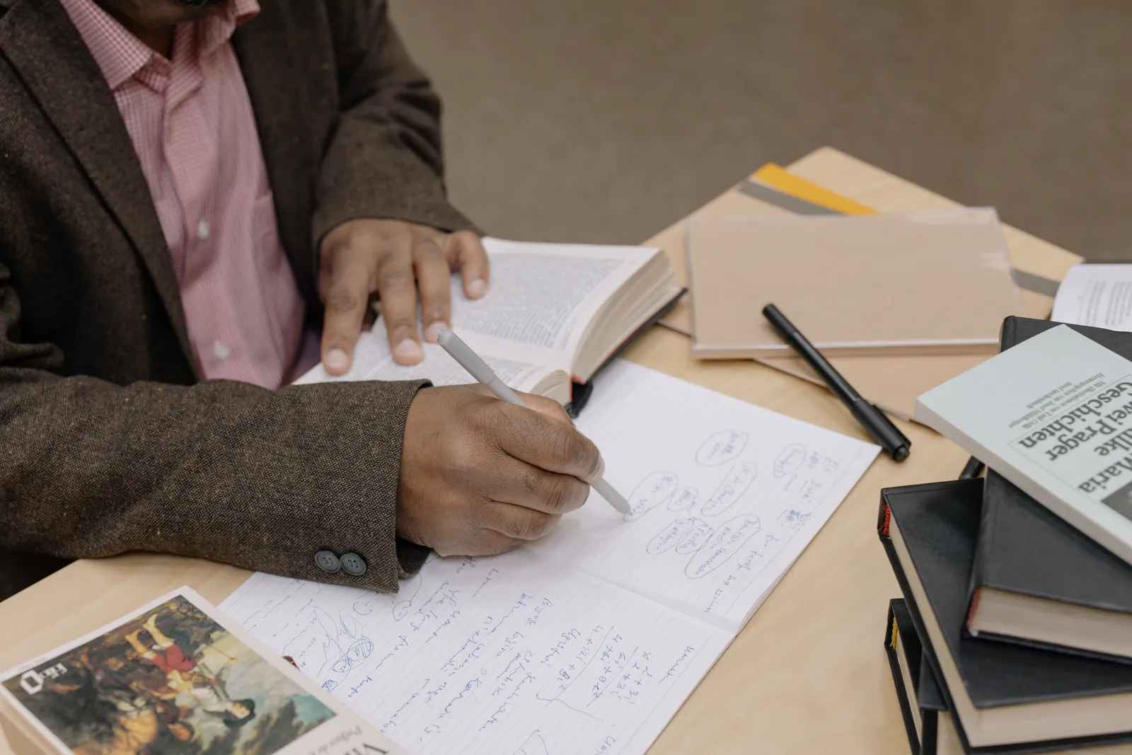 Man writing notes while researching with books at a desk indoors