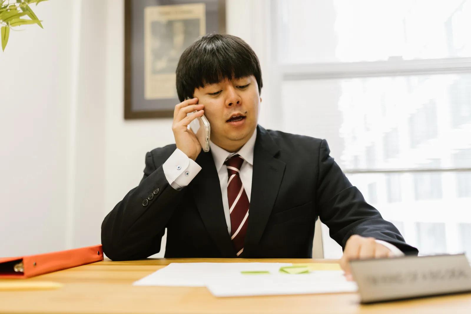 Businessman in black suit talking on phone at desk in office