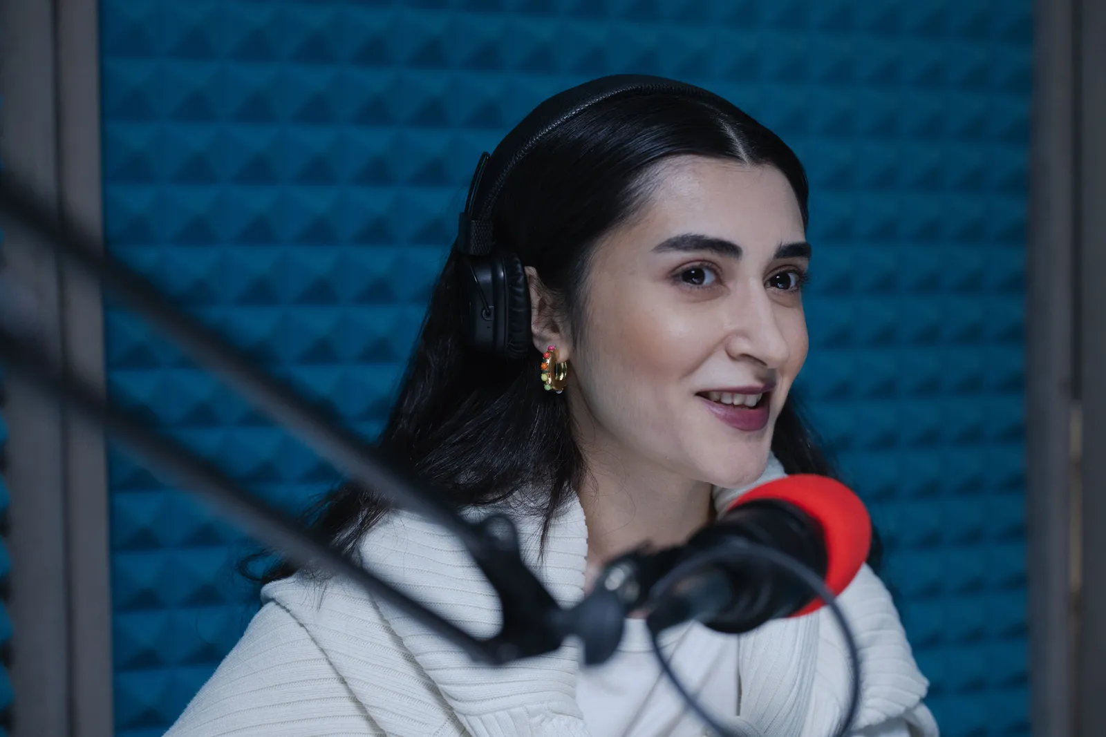 A woman with headphones speaks into a microphone in a modern podcast studio