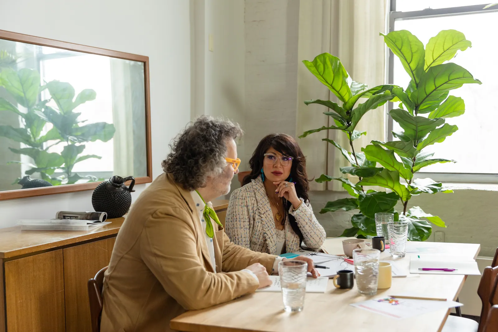 Two colleagues discussing work at a table in a plant-filled office. Bright and modern ambiance