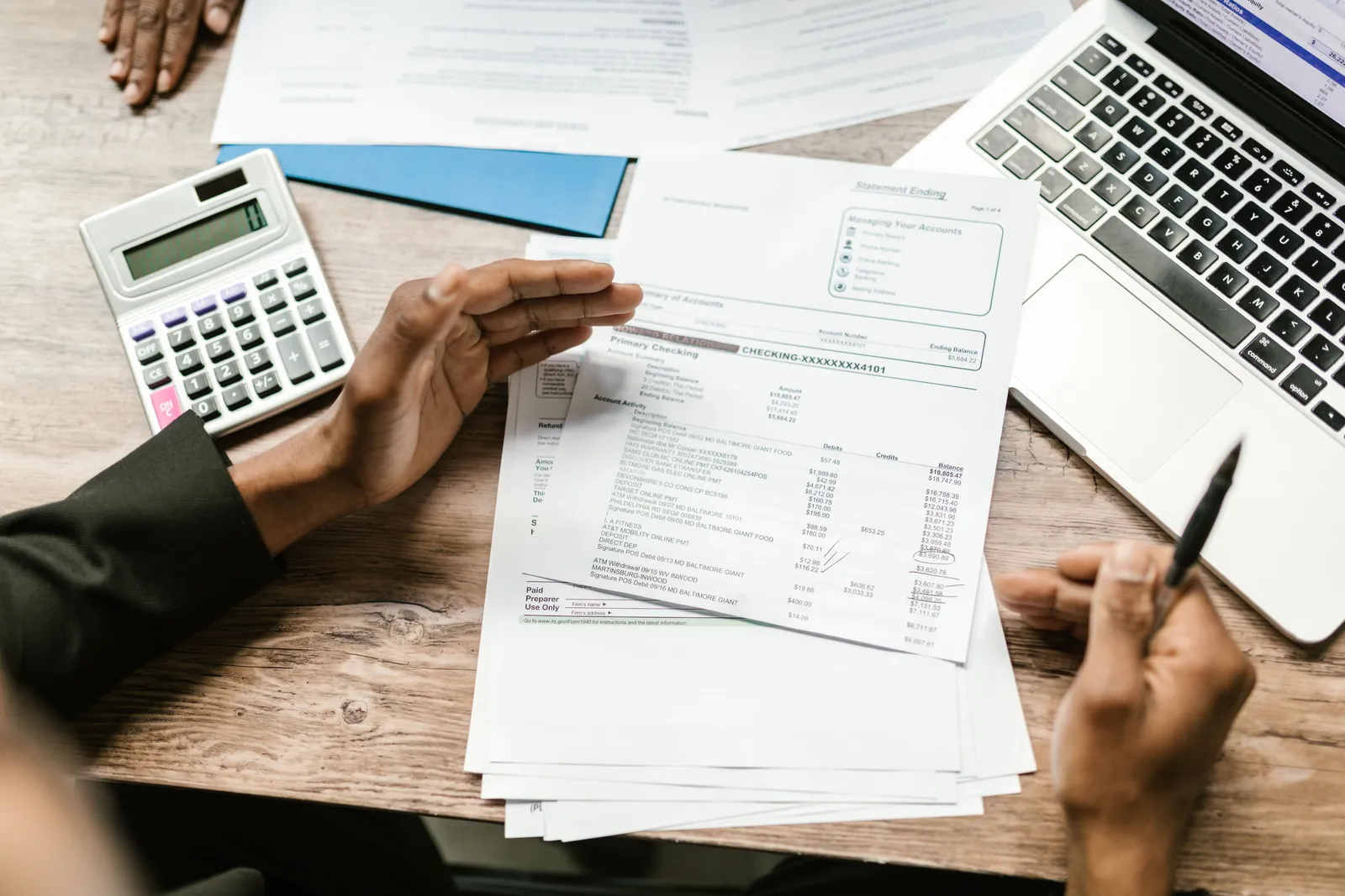 Hands holding financial documents with calculator and laptop on office desk, business analysis scene
