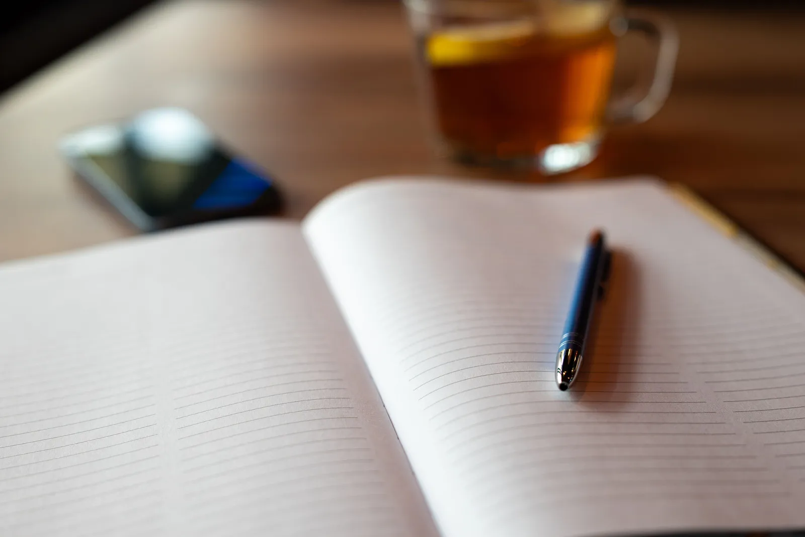An open notebook with a pen, smartphone, and tea on a wooden table. Perfect for planning and relaxing settings