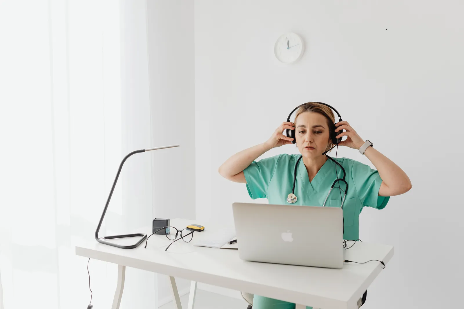 Female healthcare worker uses laptop and headphones at desk in modern office