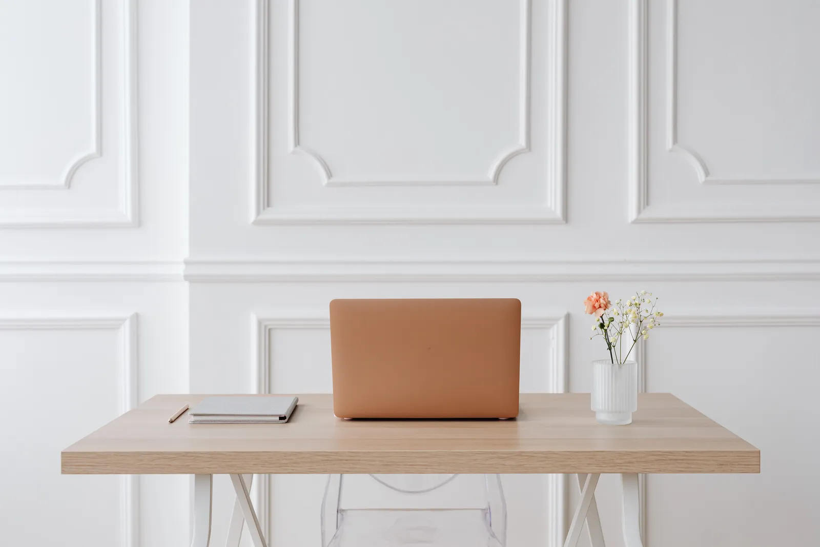 A serene workspace featuring a simple desk with a laptop, notebook, and a vase of flowers
