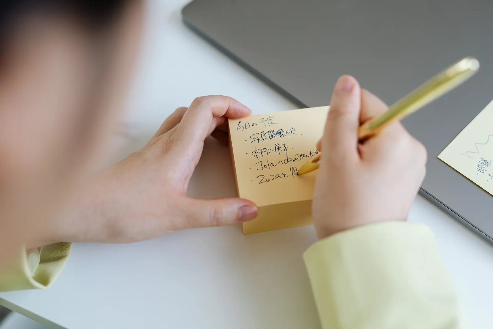 Person writing notes on sticky paper with a gold pen, taken indoors