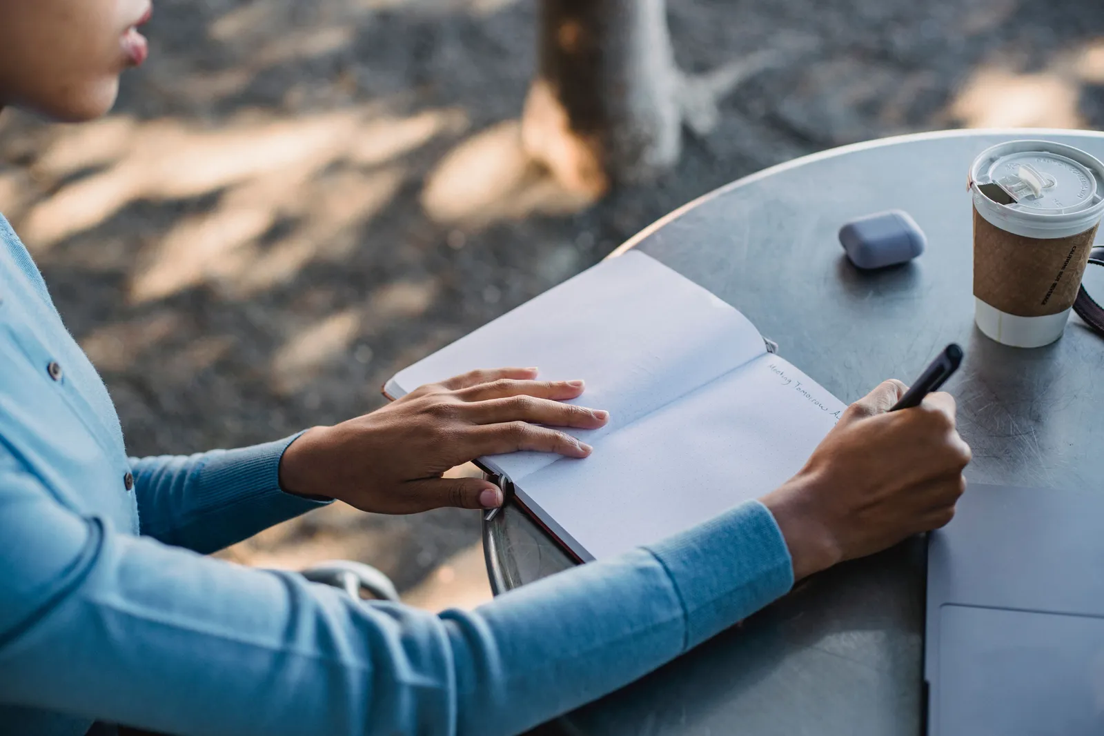 A close-up of a person writing notes in a notebook at an outdoor cafe table with a coffee cup