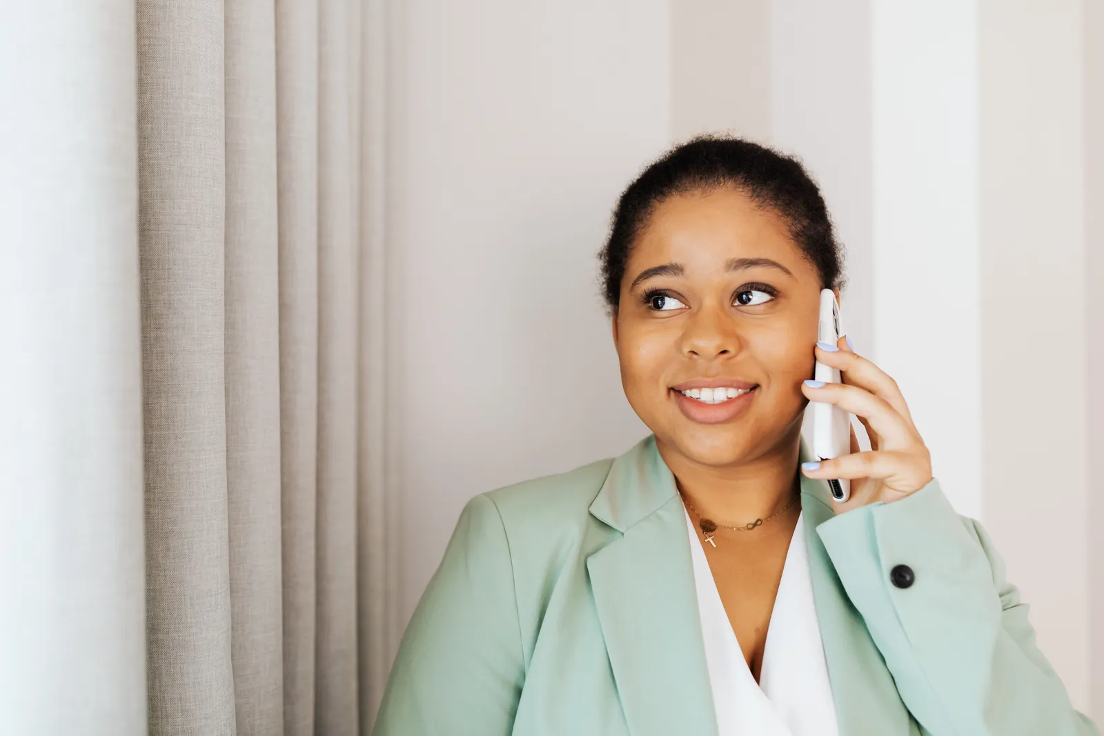 Smiling woman in blazer talking on phone indoors, expressing confidence and positivity