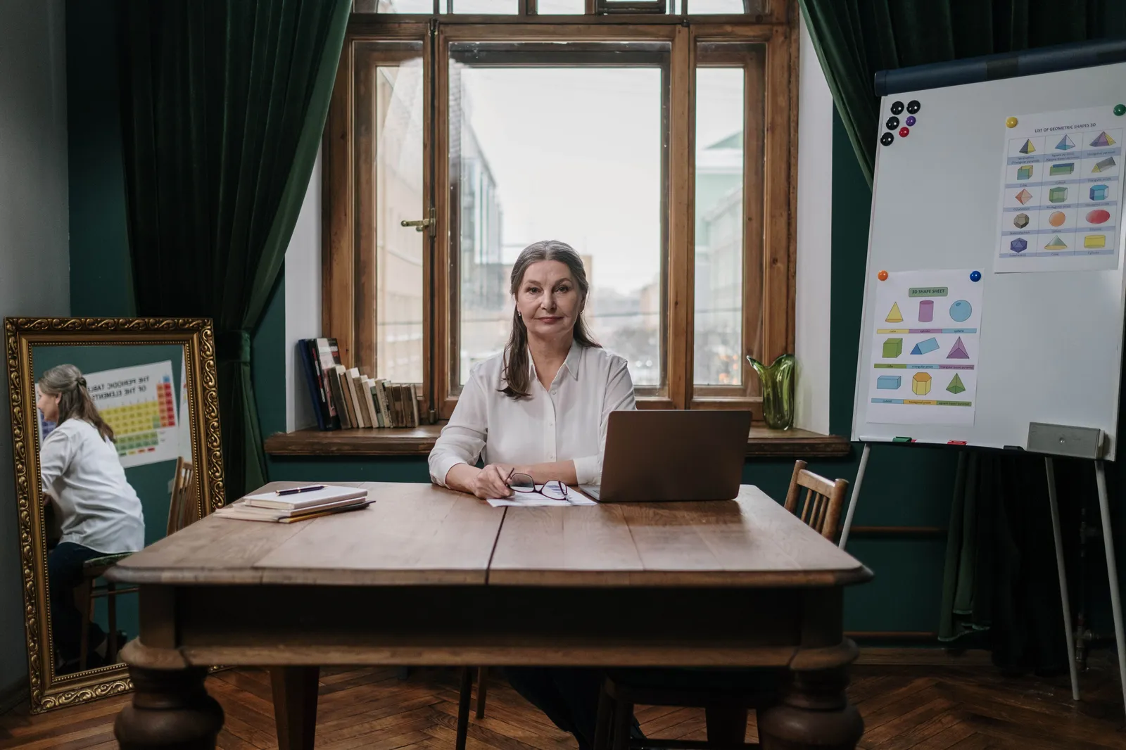 Elderly woman teaching with laptop in home office, showcasing charts and educational materials