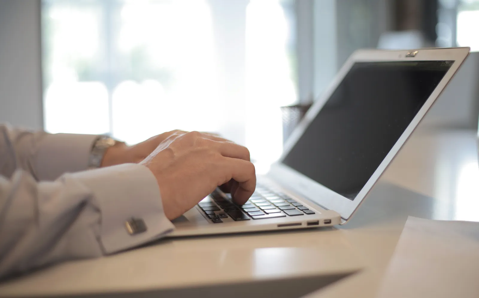 Close-up of hands typing on a laptop in a bright, modern office setting
