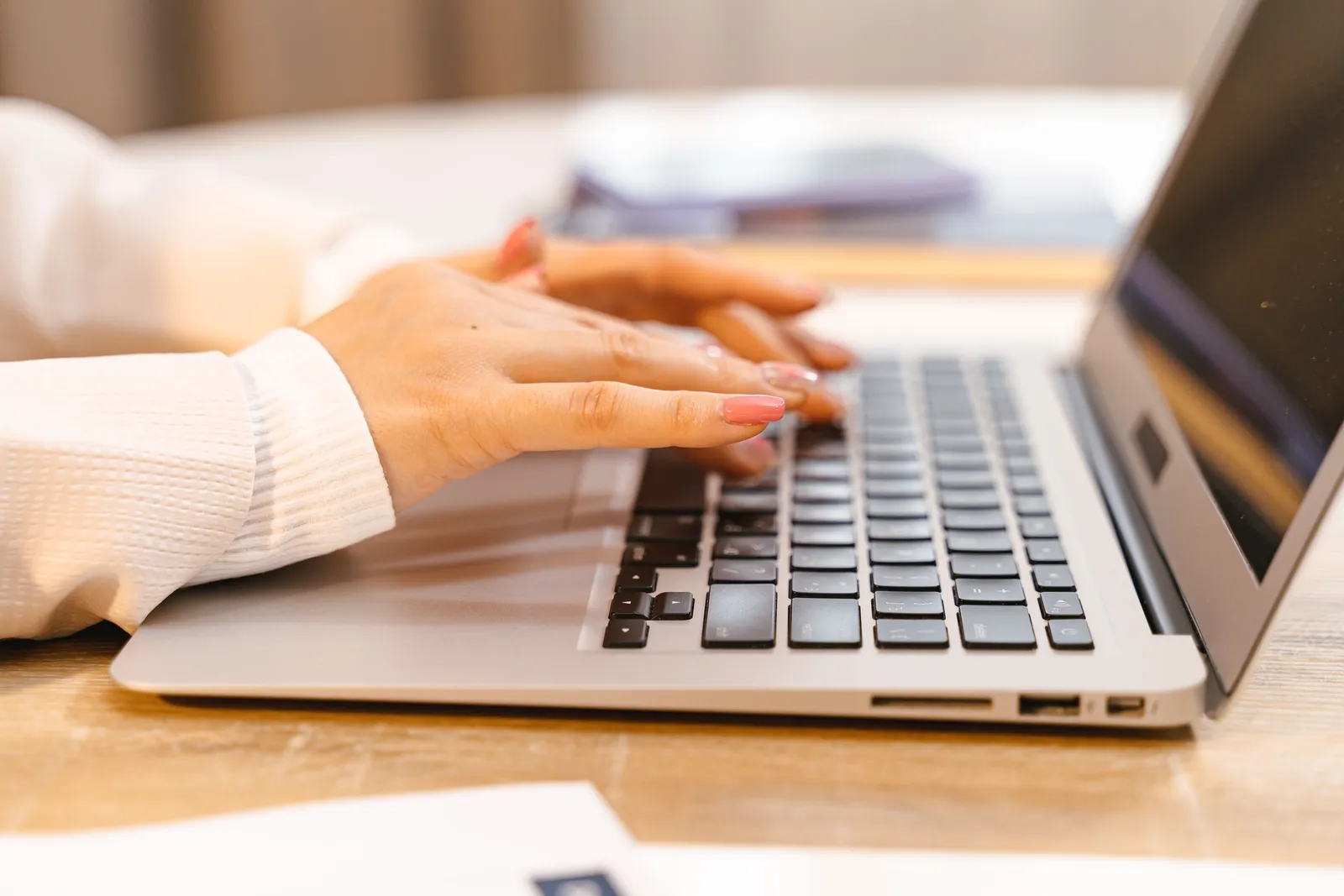A close-up view of hands typing on a laptop keyboard with a focus on manicured nails and technology