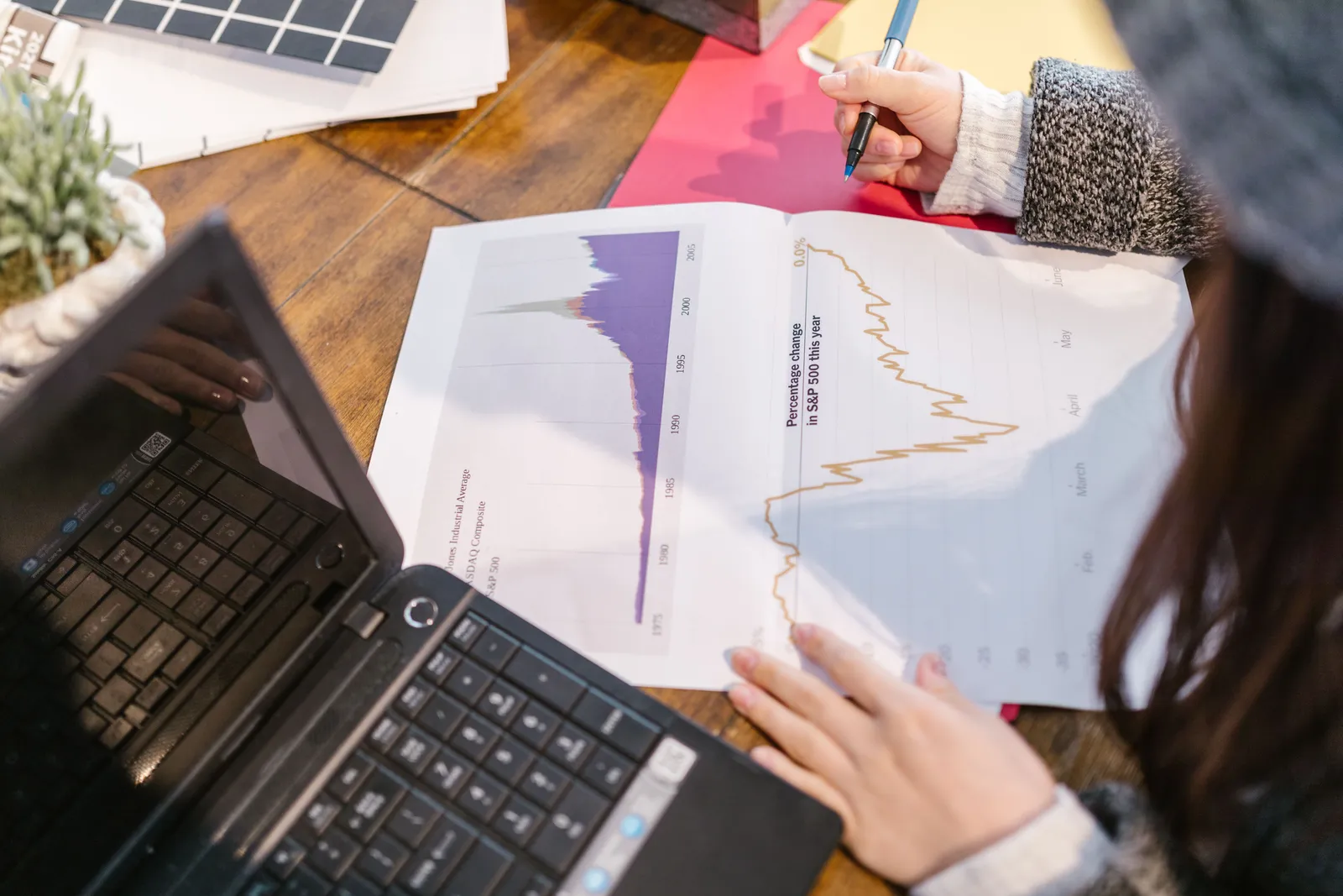 Person reviewing financial graphs and charts while taking notes beside a laptop