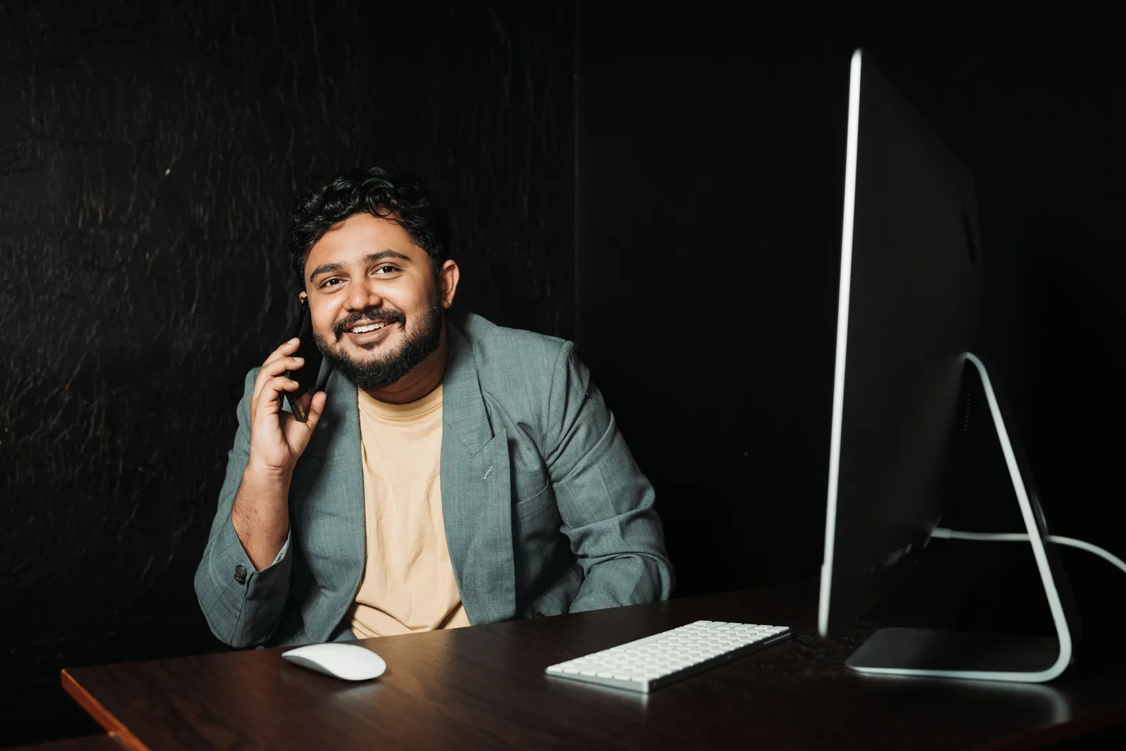 Businessman smiling while using a smartphone, seated at a desk with computer monitor