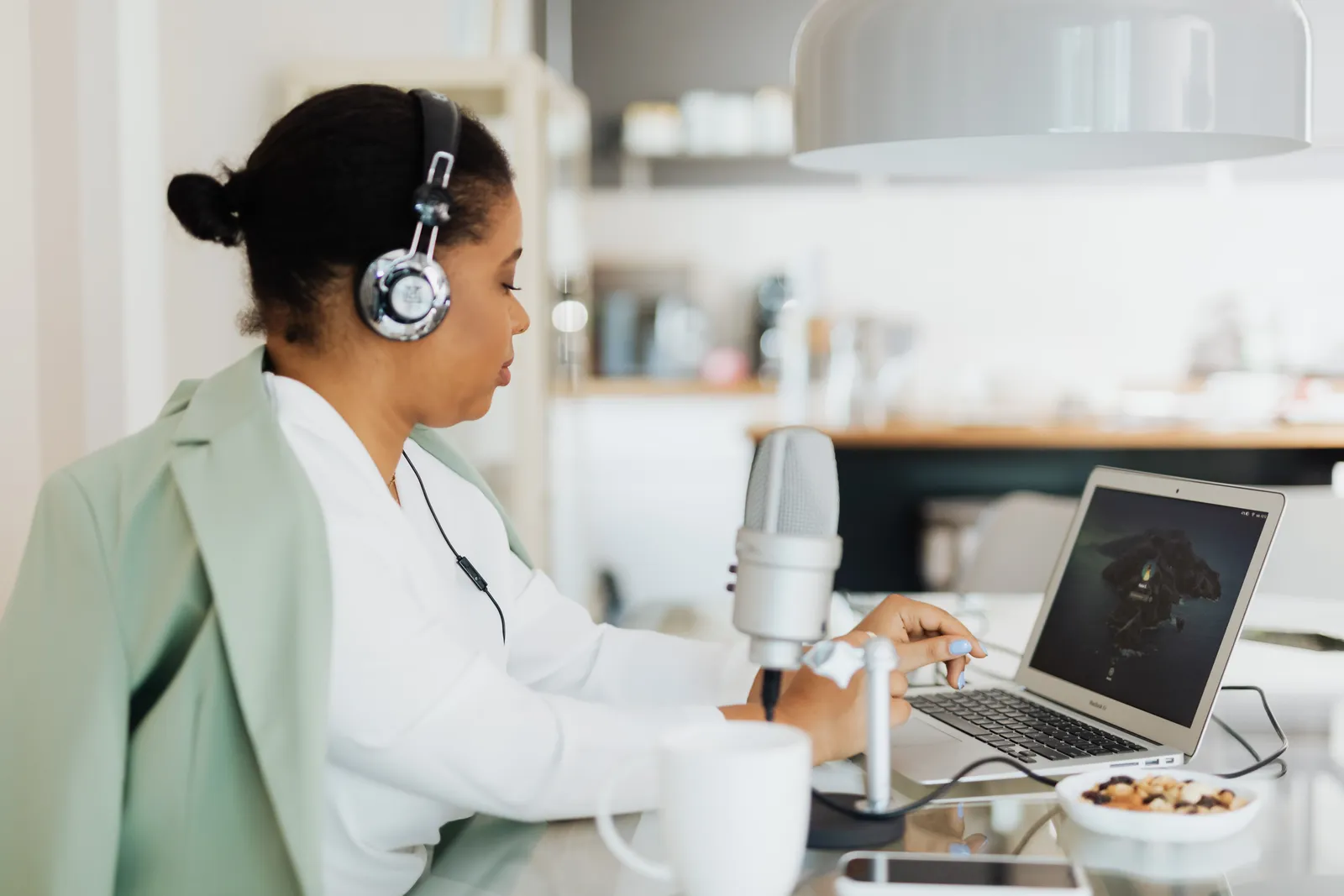 Woman using headphones and a microphone while working on a laptop indoors. Technology and lifestyle concept