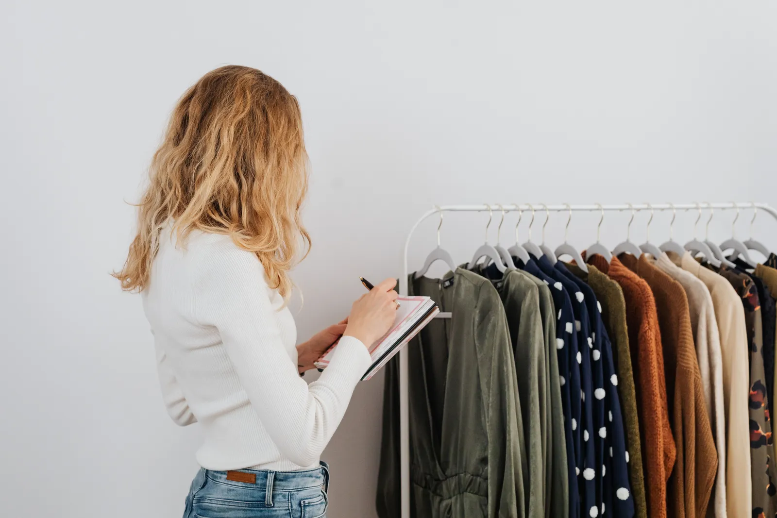 Woman writing notes checking a clothing rack with diverse fashion garments indoors