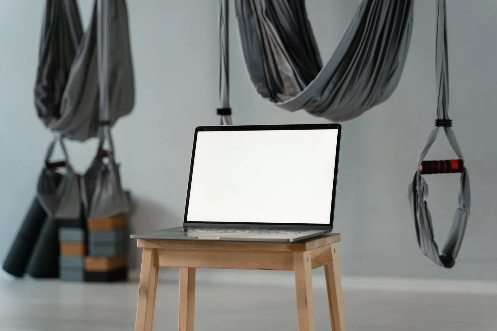 Minimalist yoga studio with aerial hammocks and blank laptop screen on a stool, ideal for diverse wellness themes