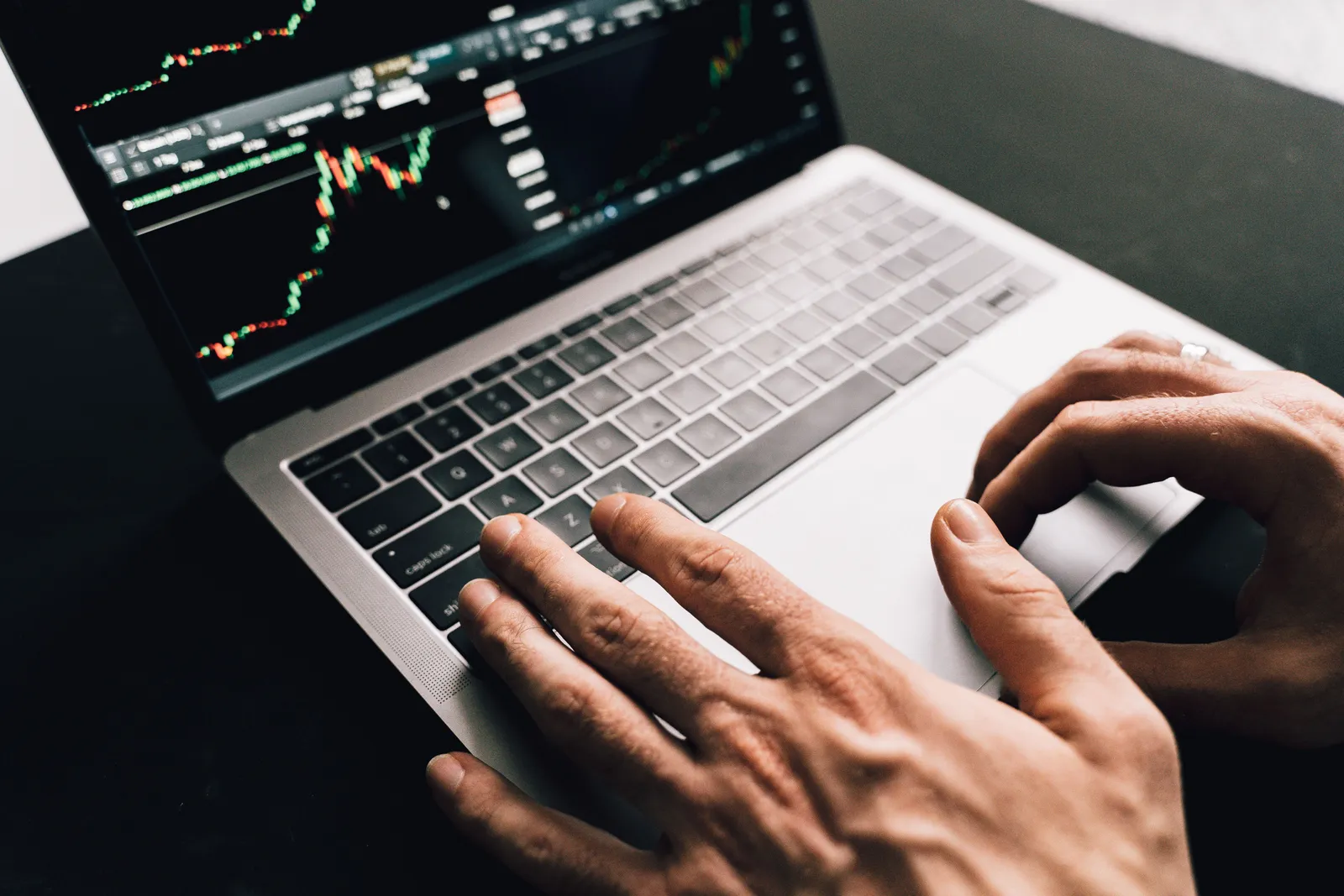 Close-up of hands typing on a laptop with stock market graphs, ideal for finance or business themes