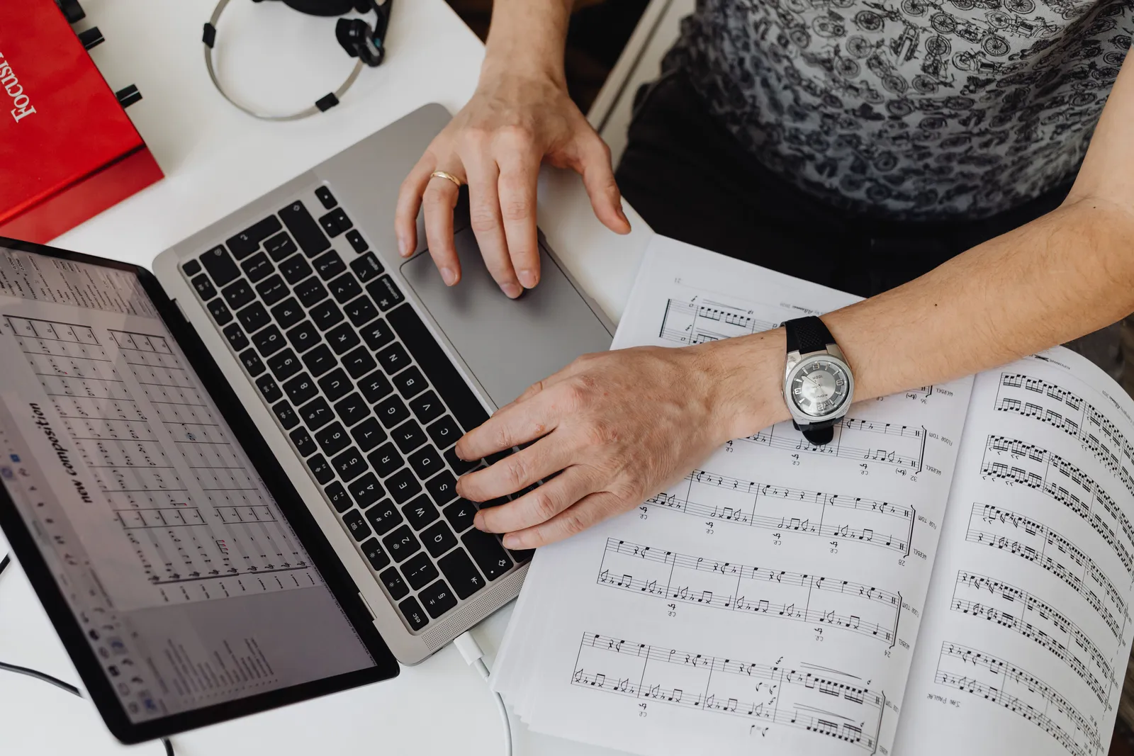 Musician working on a laptop with music sheets, creating compositions indoors at a desk