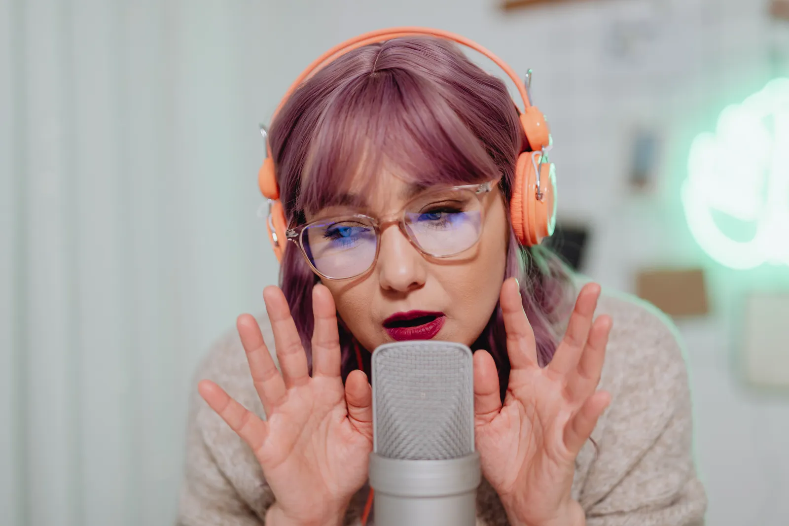 A woman with pink hair and headphones recording ASMR using a microphone indoors