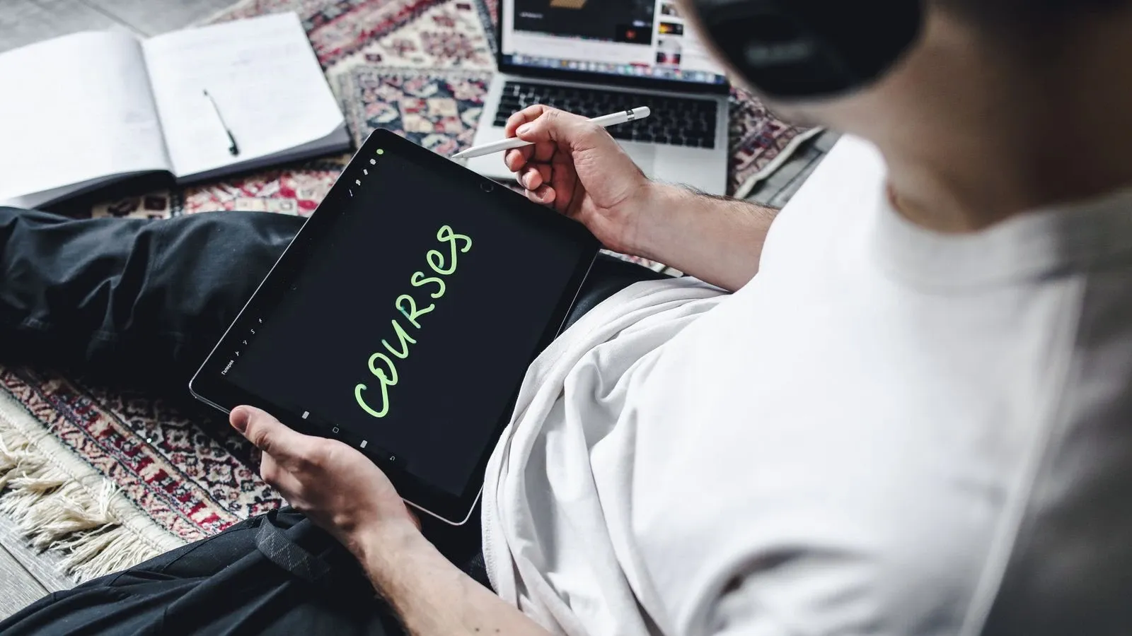 A learner using a tablet beside headphones and a notebook