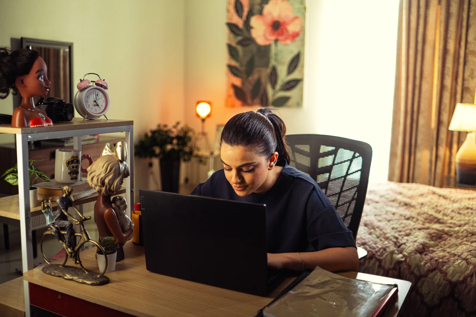 A woman focusing on her laptop in a cozy home office surrounded by decor and warm lighting