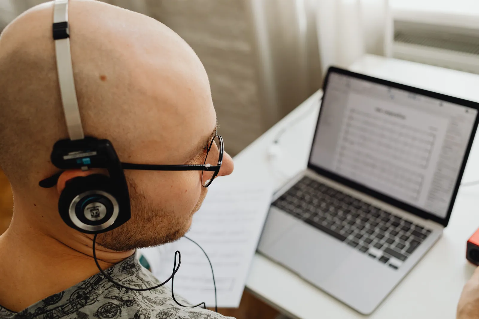 Bald man in headphones working on a laptop, focused on tasks