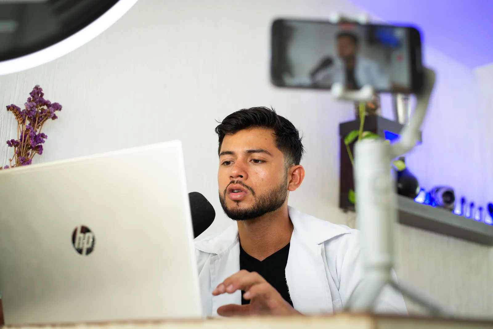 A young man works on a laptop while streaming content online with a smartphone