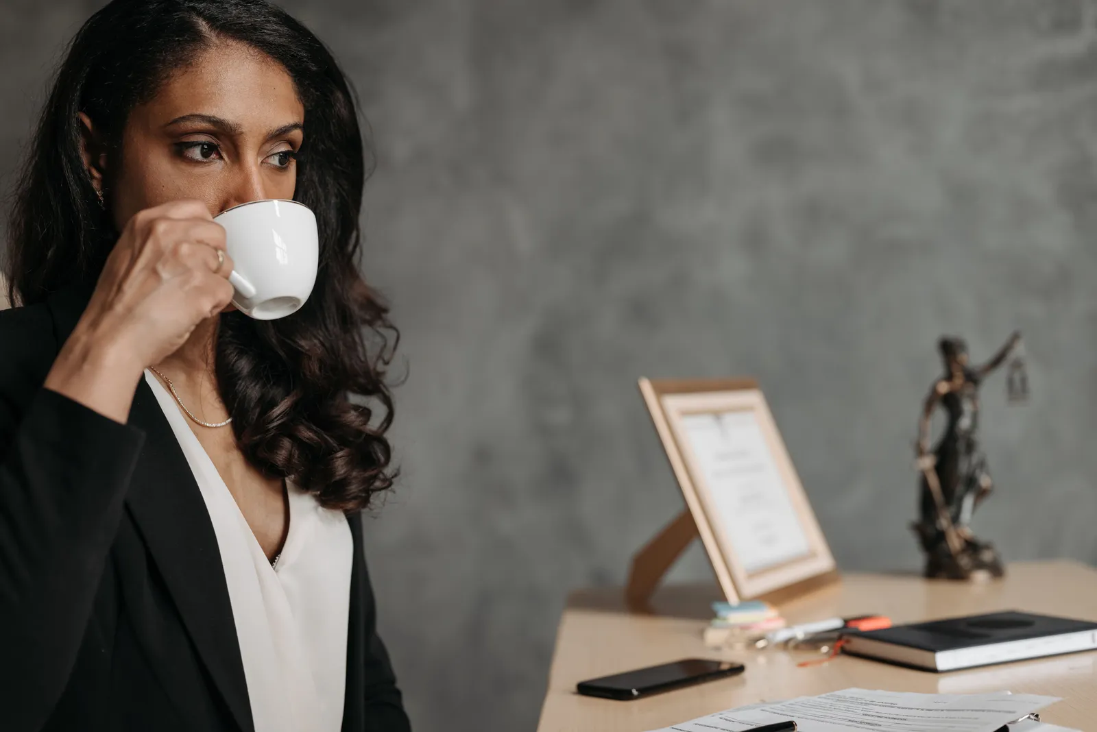 A focused professional woman drinks coffee at her desk in an office setting